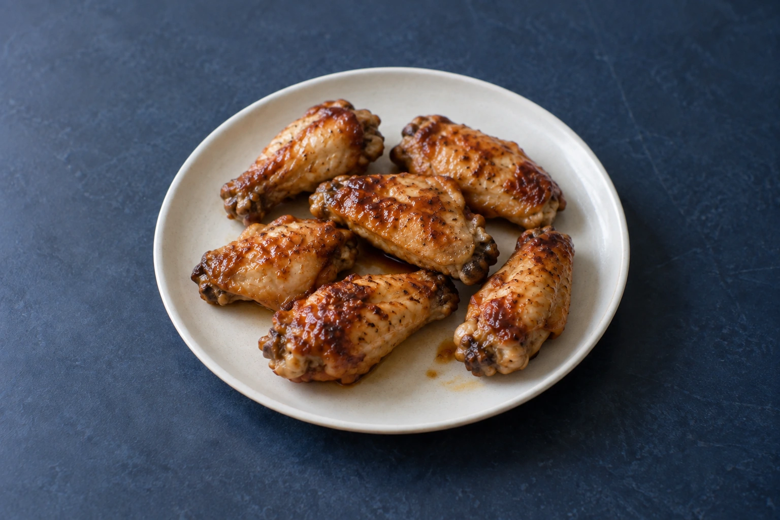 Six lightly glazed chicken wing pieces on a cream plate on a navy tabletop